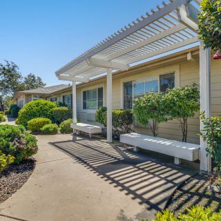 A sunny garden area with a pergola, benches, and well-maintained shrubbery.