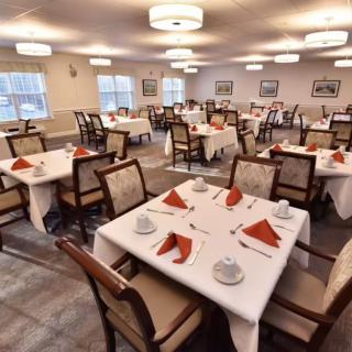 A well-lit dining room with tables neatly set, featuring folded napkins and comfortable chairs.