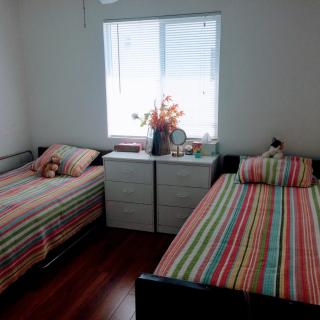 A cozy bedroom with twin beds featuring colorful striped bedding, a dresser with decorative items, and a bright window illuminating the space.