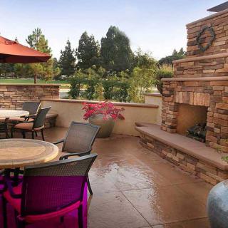 A cozy outdoor patio with a brick fireplace, comfortable seating, and surrounding greenery.