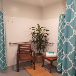 A bathroom shower area with teal patterned curtains, featuring a wooden bench, potted plant, and neatly folded towels.
