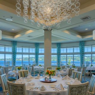 Elegant dining room with beautifully set round tables and a stunning view of the water.