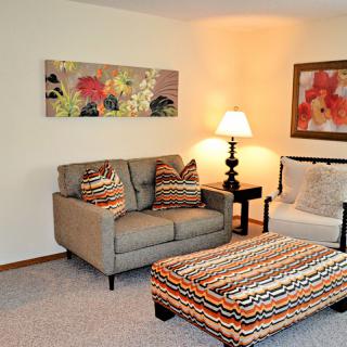 A cozy living room with a sofa, colorful ottoman, and wall art.