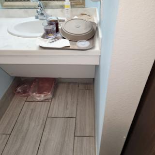 A cluttered bathroom countertop with a sink, plates, and some items on the floor.
