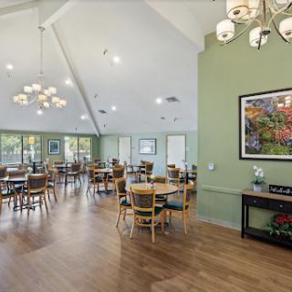 A spacious dining area with wooden floors, green walls, and modern chandeliers, featuring tables and chairs arranged for a welcoming atmosphere.