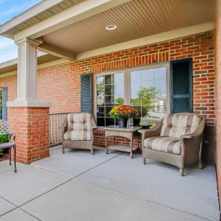 A cozy porch with comfortable seating, decorated with flowers and set against a brick exterior.