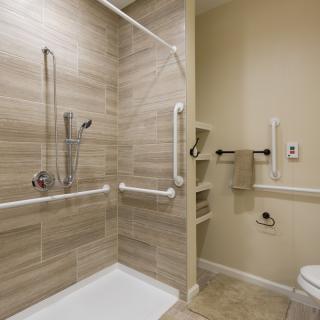 An accessible bathroom featuring a shower with grab bars and a tiled wall.