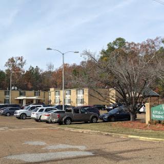 A view of an apartment complex with a parking lot filled with various vehicles and trees in the background.