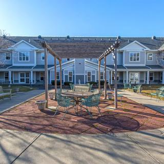 A sunny outdoor patio area with seating under a pergola in front of residential buildings.