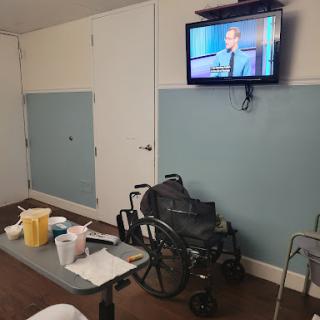 A view of a hospital room featuring a wheelchair, medical supplies on a table, and a television.