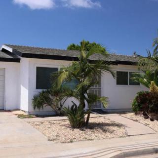 A single-story white house with a palm tree in the front yard on a sunny day.