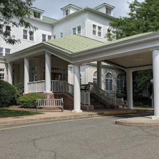 A charming hotel entrance featuring a green roof and elegant pillars, surrounded by lush greenery.