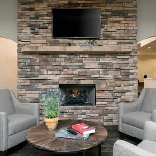 A cozy living room with a stone fireplace, armchairs, and a television mounted above.