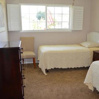 A cozy bedroom featuring twin beds, a dresser, and a window with shutters.