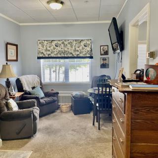 A cozy living room with comfortable seating, a wall-mounted television, and a window adorned with floral curtains.