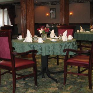 A cozy dining room with elegantly set tables, featuring folded napkins and polished wooden chairs.