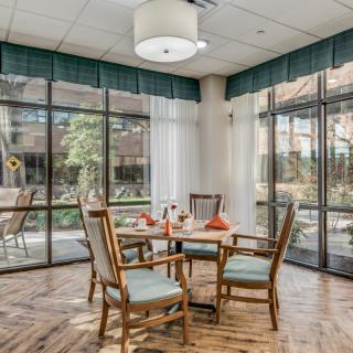 A cozy dining area with a table and four wooden chairs, surrounded by large windows letting in natural light.