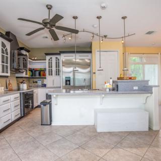 A modern kitchen with white cabinetry and a spacious island, featuring pendant lighting and tile flooring.