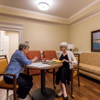 Two people engaged in a conversation at a table in a cozy room.
