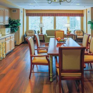 A spacious dining room with a large table, elegant chairs, and warm hardwood floors, featuring a kitchen area and large windows that allow natural light to fill the space.
