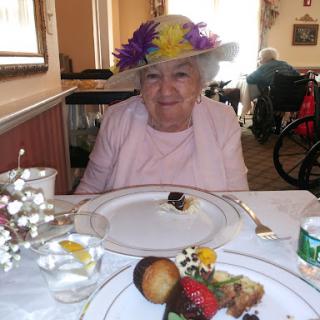 A joyful elderly woman wearing a colorful hat, enjoying a festive meal with dessert.