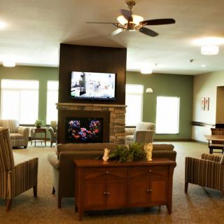 A cozy living area featuring a television above a fireplace, surrounded by comfortable seating and warm lighting.