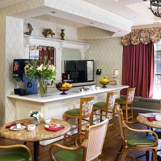 A cozy cafe interior with tables and chairs arranged around a bar, featuring a television and decorative flowers.