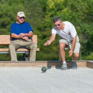Two men playing bocce outdoors on a sunny day.