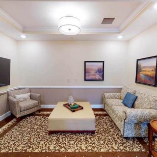 A cozy living room with a sofa, armchair, and coffee table, adorned with artwork and a patterned carpet.