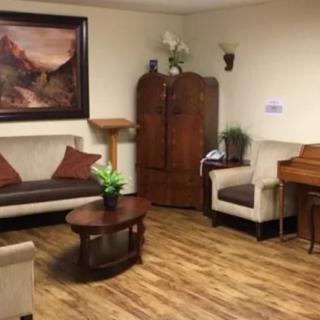A cozy living room with a sofa, armchair, coffee table, and piano, featuring warm decor and wooden flooring.