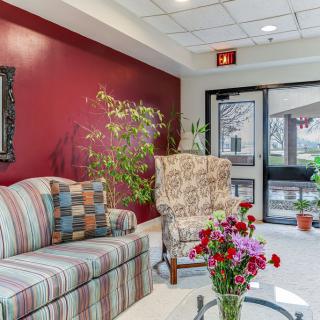 A cozy lobby with a striped sofa, patterned armchair, and vibrant plants and flowers.