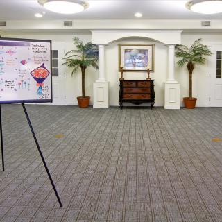 A spacious conference room with an easel displaying a presentation, flanked by potted plants and elegant decor.
