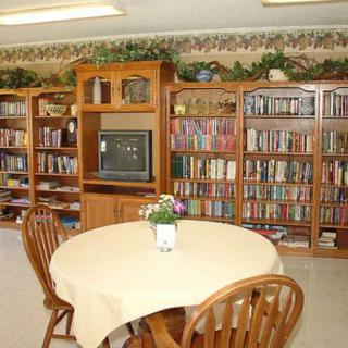 A cozy library corner with wooden bookshelves filled with books, a table with chairs, and a small television.