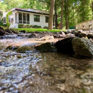 A tranquil scene featuring a house by a flowing stream, surrounded by lush greenery.