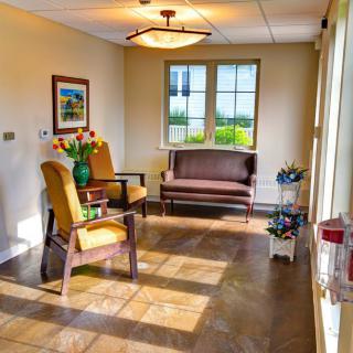 A cozy waiting room with chairs, a table, and sunlight streaming through the window.