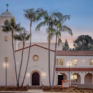 A Mediterranean-style church surrounded by palm trees, captured during the evening.