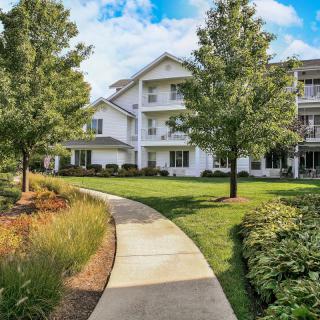 A scenic view of a residential building with a winding pathway surrounded by lush greenery and trees.
