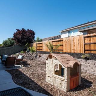 A sunny backyard with a small playhouse and patio seating area.