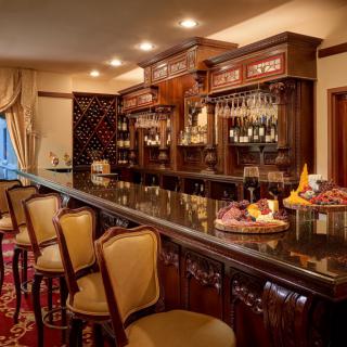 A cozy bar with an elegant wooden counter and seating, adorned with shelves of bottles and glasses.