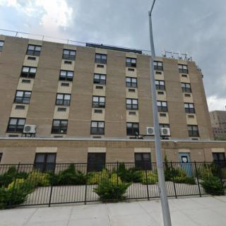 A street view of a multi-story residential apartment building with several windows and a fenced entrance.
