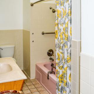A bathroom featuring a bathtub with a floral shower curtain, a toilet, and a sink area.
