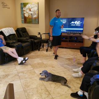 A group of people relaxing in a living room with a dog lying on the floor.