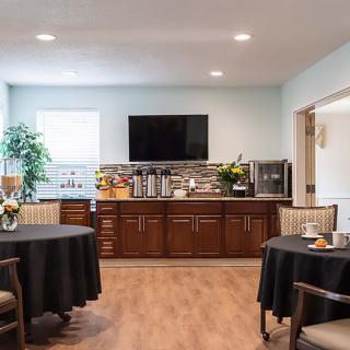 A modern dining area with round tables, chairs, and a television mounted above wooden cabinets.