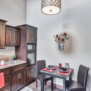 A cozy kitchen nook with a small dining table set for two, surrounded by modern wood-finished cabinets and a stylish hanging light fixture.