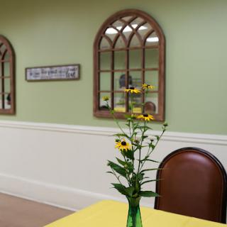 A cozy dining area featuring a cheerful yellow tablecloth and a vase of sunflowers, complemented by green walls and decorative mirrors.