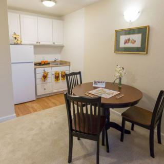 A cozy dining area with a small kitchenette featuring white cabinets and a table with chairs.