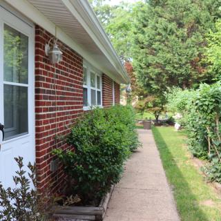 A brick house with a pathway lined by bushes and greenery.
