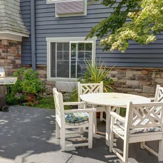 A cozy patio area with a round table and white chairs surrounded by plants and a stone facade.