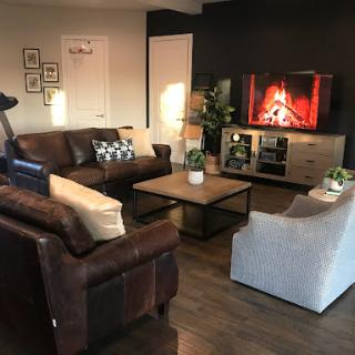 A cozy living room featuring a comfortable sofa, an armchair, and a television displaying a fireplace.