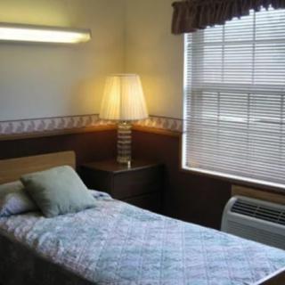 A simple bedroom with a single bed, a bedside lamp, and a window with blinds.